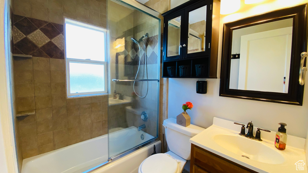 Full bathroom with toilet, bath / shower combo with glass door, and vanity