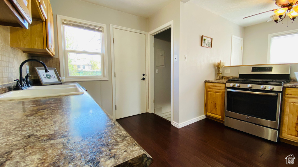 Kitchen with dark hardwood / wood-style floors, stainless steel gas range, ceiling fan, and tasteful backsplash
