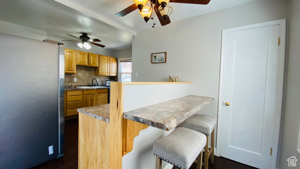Kitchen with kitchen peninsula, ceiling fan, tasteful backsplash, stainless steel fridge, and sink