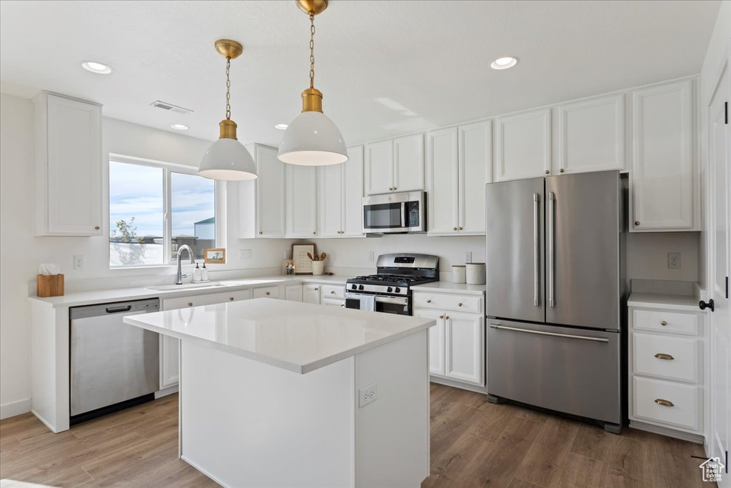 Kitchen with hardwood / wood-style floors, stainless steel appliances, white cabinetry, and decorative light fixtures