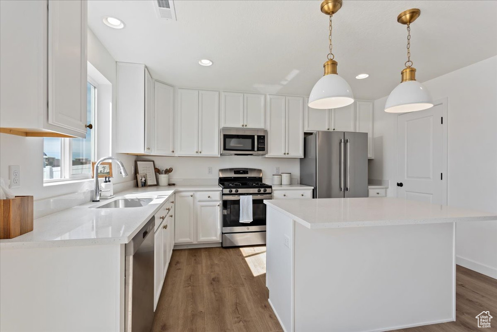 Kitchen with white cabinetry, hardwood / wood-style floors, stainless steel appliances, sink, and a kitchen island