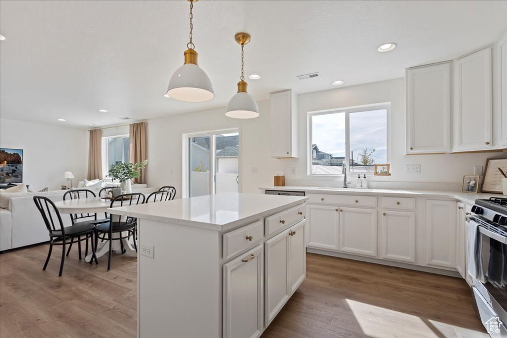 Kitchen featuring a center island, decorative light fixtures, light hardwood / wood-style flooring, white cabinetry, and stainless steel gas range