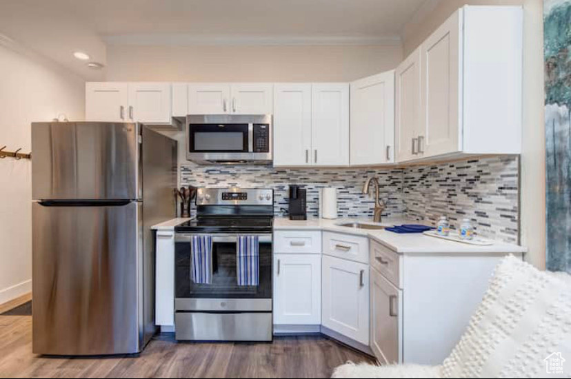 Kitchen featuring wood-type flooring, white cabinets, appliances with stainless steel finishes, sink, and tasteful backsplash