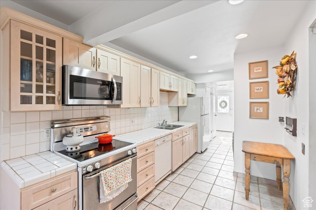 Kitchen featuring backsplash, tile counters, white appliances, and light tile floors