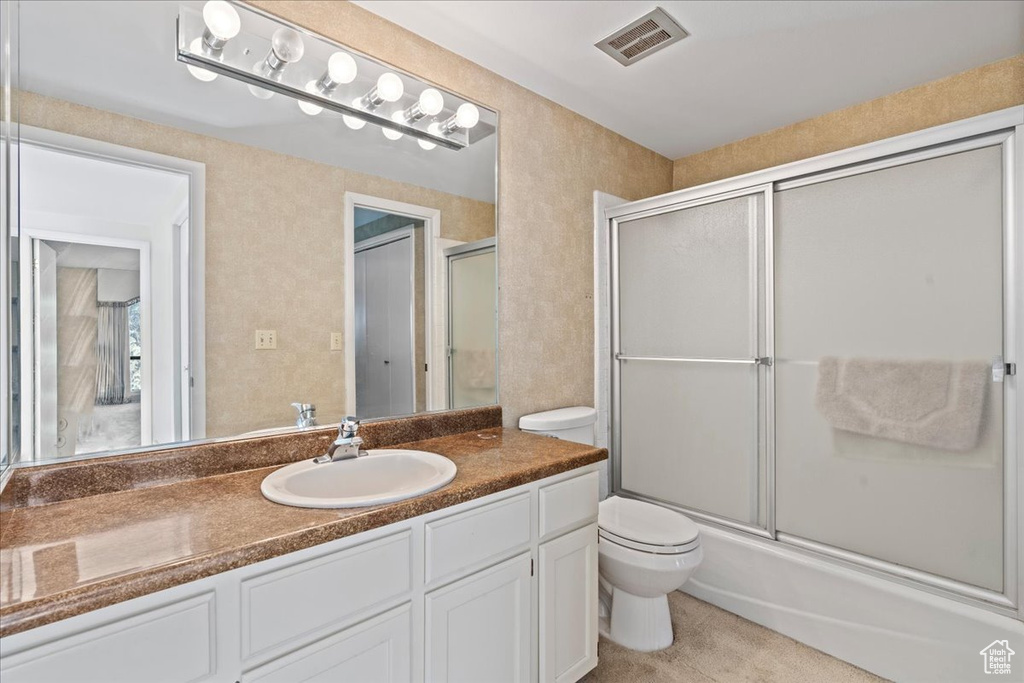 Full bathroom with large vanity, toilet, and bath / shower combo with glass door