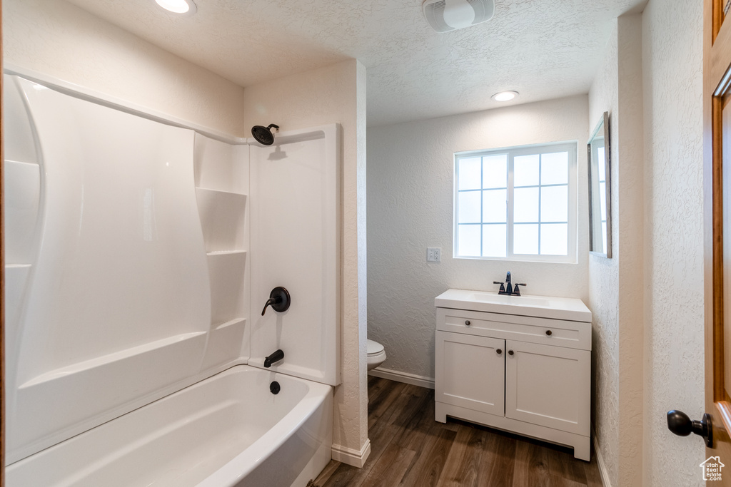 Full bathroom with vanity, hardwood / wood-style floors, shower / bath combination, toilet, and a textured ceiling