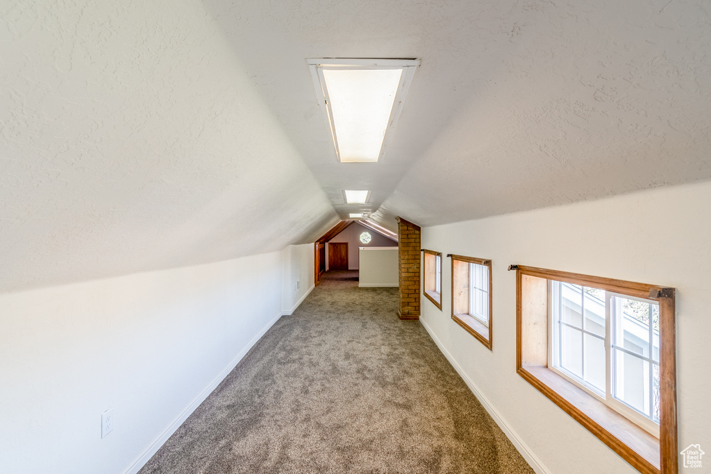 Additional living space featuring vaulted ceiling, brick wall, and carpet floors