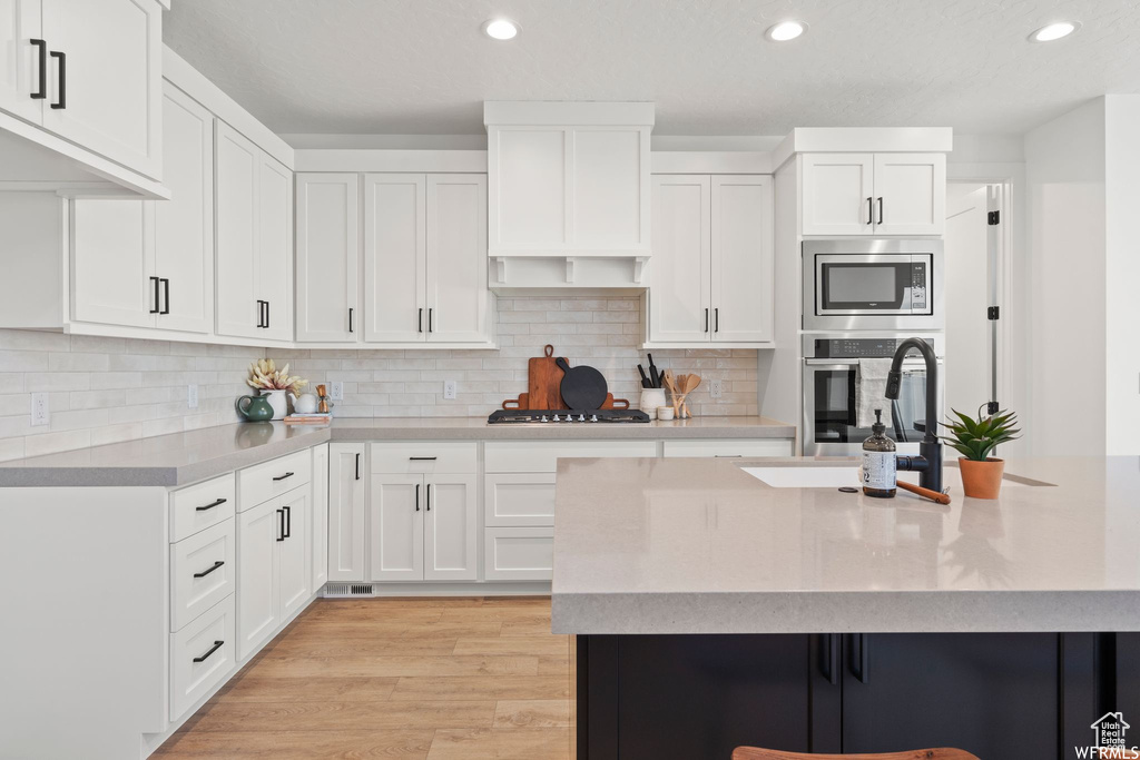 Kitchen featuring white cabinetry, backsplash, stainless steel appliances, and light hardwood / wood-style floors