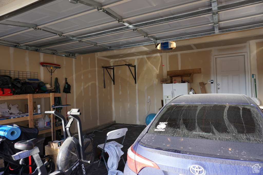 Garage featuring white refrigerator with ice dispenser and a garage door opener