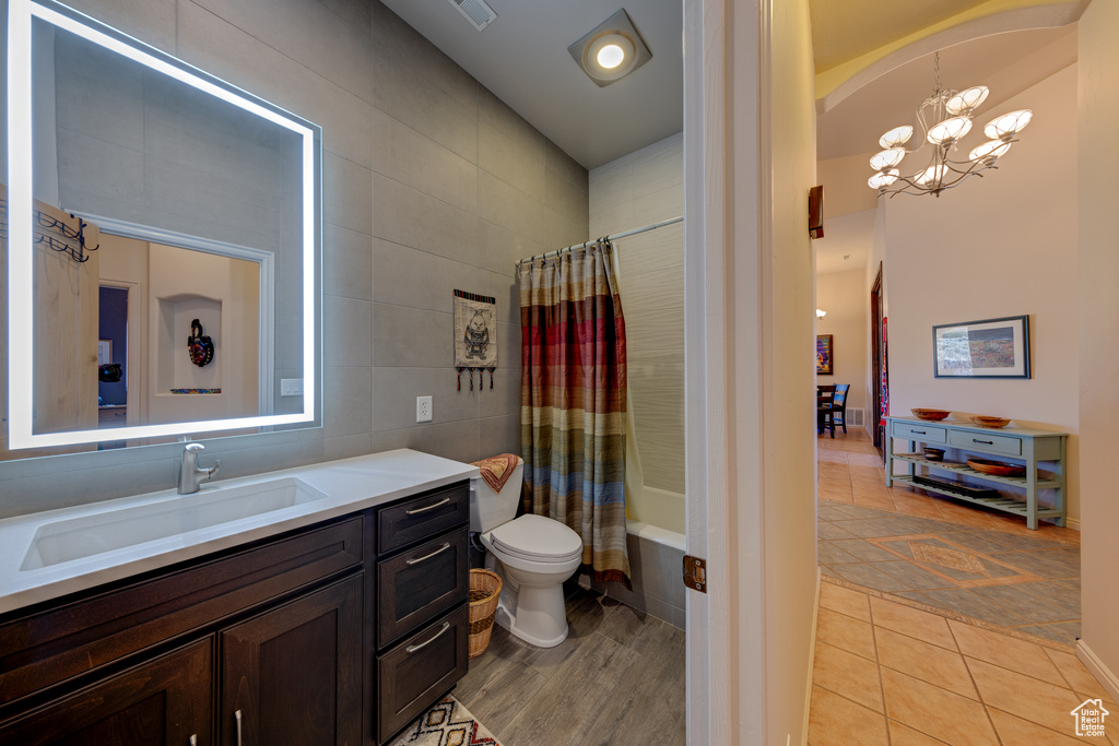 Full bathroom with tile walls, large vanity, shower / bath combo with shower curtain, toilet, and an inviting chandelier