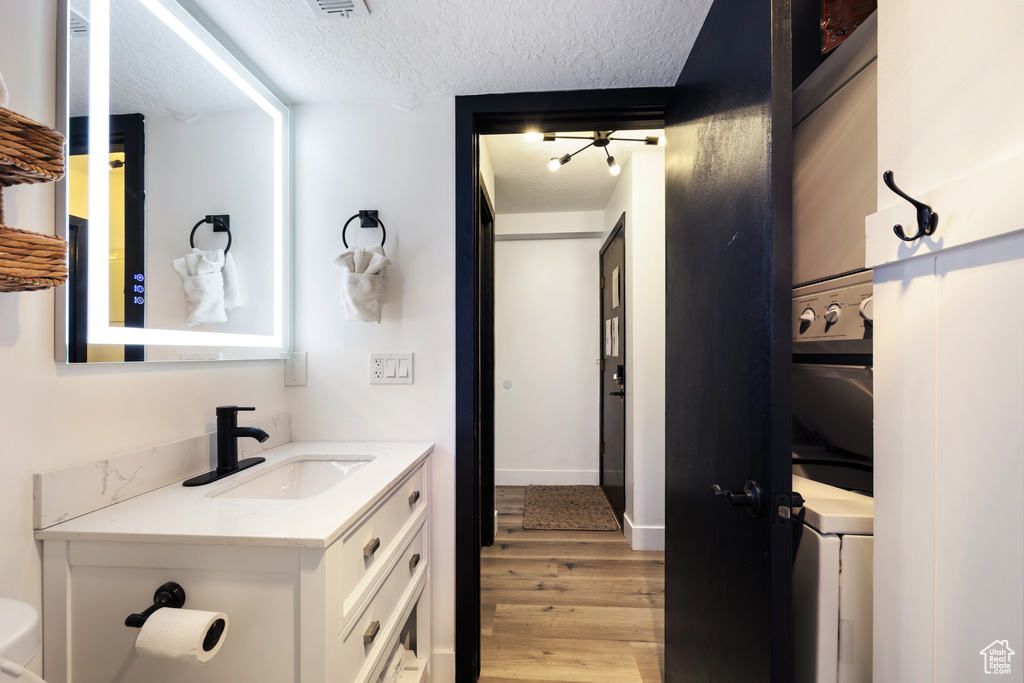 Bathroom with a textured ceiling, stacked washer and dryer, toilet, wood-type flooring, and vanity
