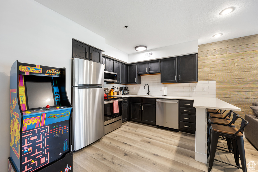 Kitchen featuring backsplash, sink, stainless steel appliances, and light wood-type flooring