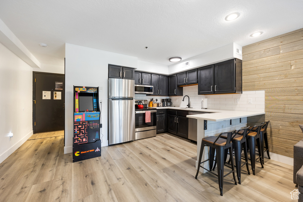 Kitchen featuring kitchen peninsula, a kitchen bar, backsplash, stainless steel appliances, and light wood-type flooring