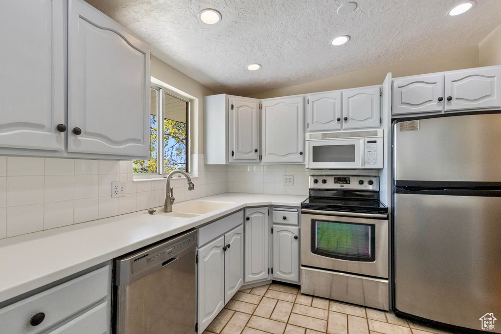 Kitchen featuring appliances with stainless steel finishes, white cabinets, backsplash, and light tile floors