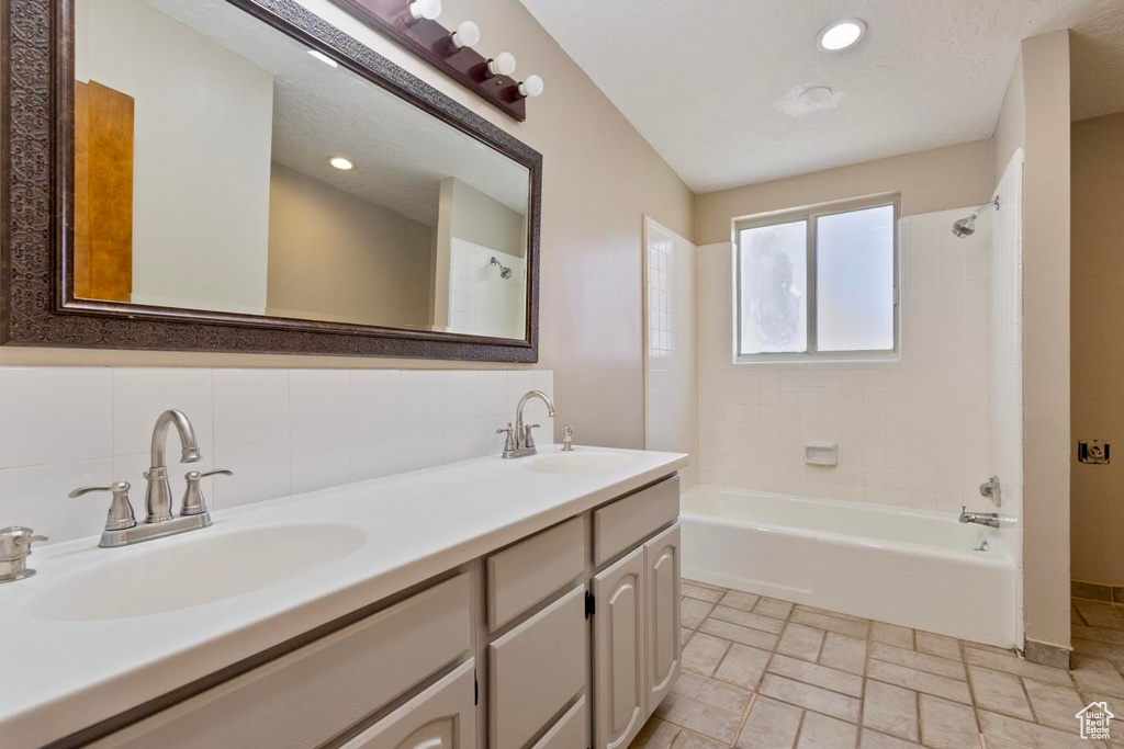 Bathroom with tasteful backsplash, tiled shower / bath, tile floors, and double sink vanity