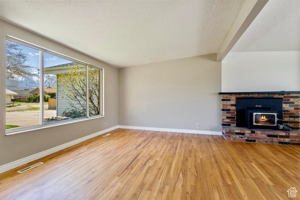 Unfurnished living room with beamed ceiling, a brick fireplace, and light wood-type flooring
