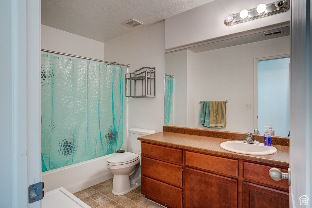 Full bathroom with tile flooring, large vanity, a textured ceiling, shower / bath combo, and toilet