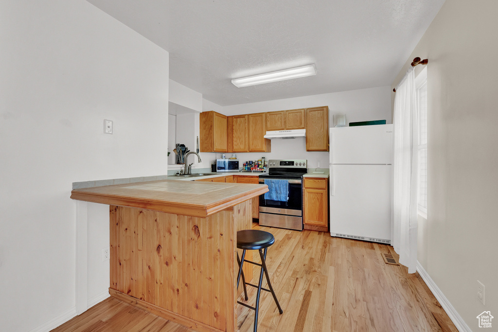 Kitchen featuring a kitchen breakfast bar, kitchen peninsula, stainless steel appliances, sink, and light hardwood / wood-style floors