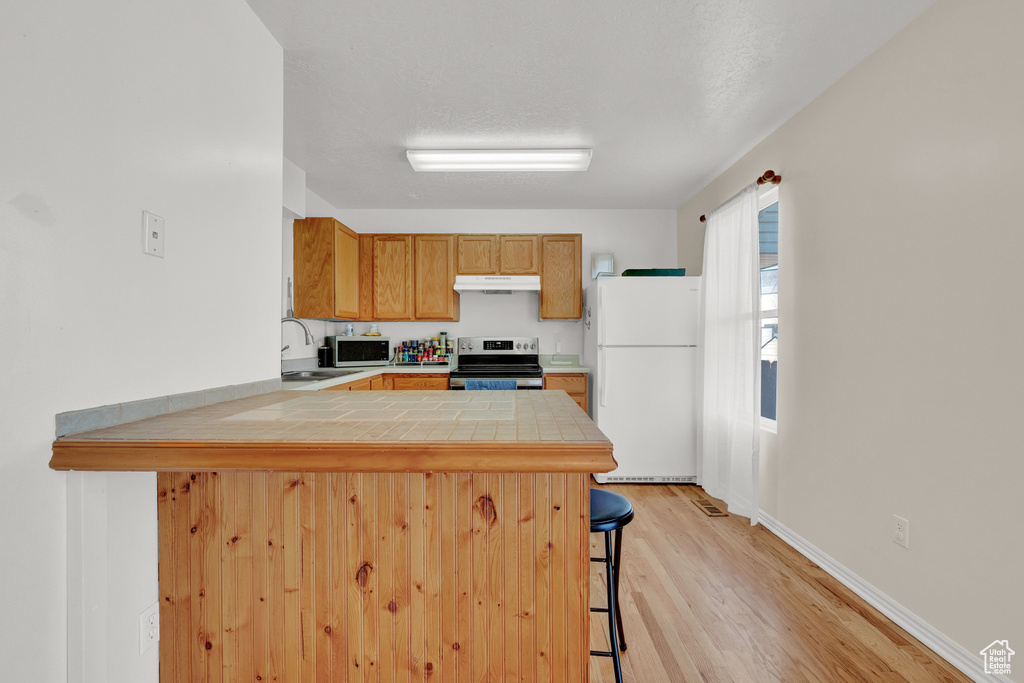 Kitchen featuring light wood-type flooring, kitchen peninsula, stainless steel appliances, sink, and a breakfast bar area
