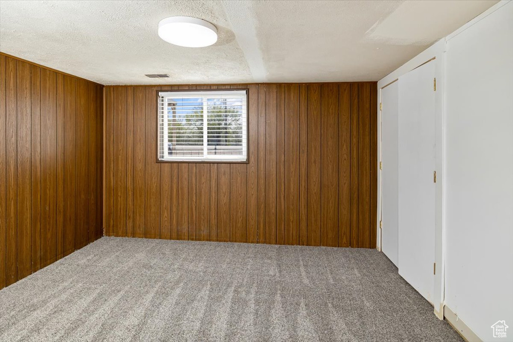 Carpeted spare room featuring a textured ceiling and wooden walls