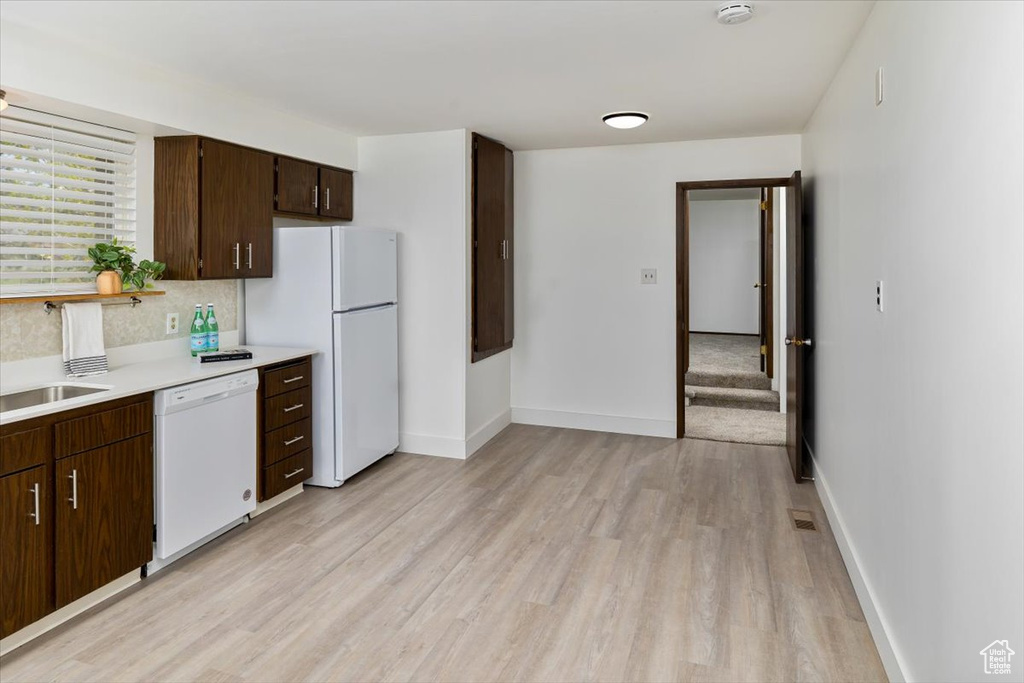 Kitchen with white appliances, light wood-type flooring, sink, tasteful backsplash, and dark brown cabinetry