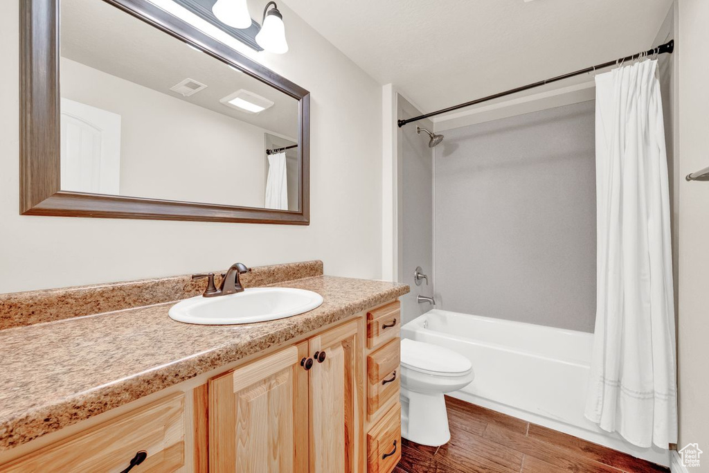 Full bathroom featuring wood-type flooring, toilet, oversized vanity, and shower / tub combo with curtain