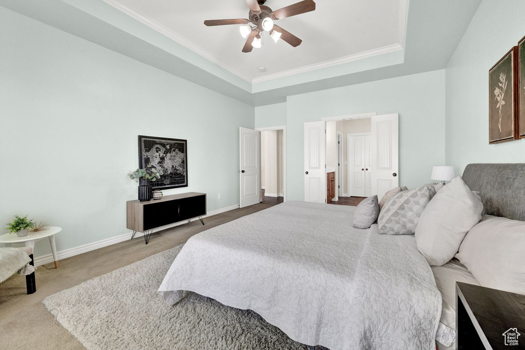 Carpeted bedroom featuring ornamental molding, ceiling fan, and a tray ceiling