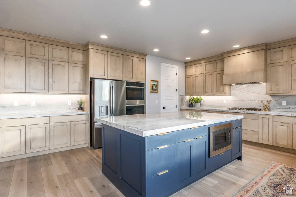 Kitchen featuring light stone counters, appliances with stainless steel finishes, custom exhaust hood, a kitchen island, and light wood-type flooring