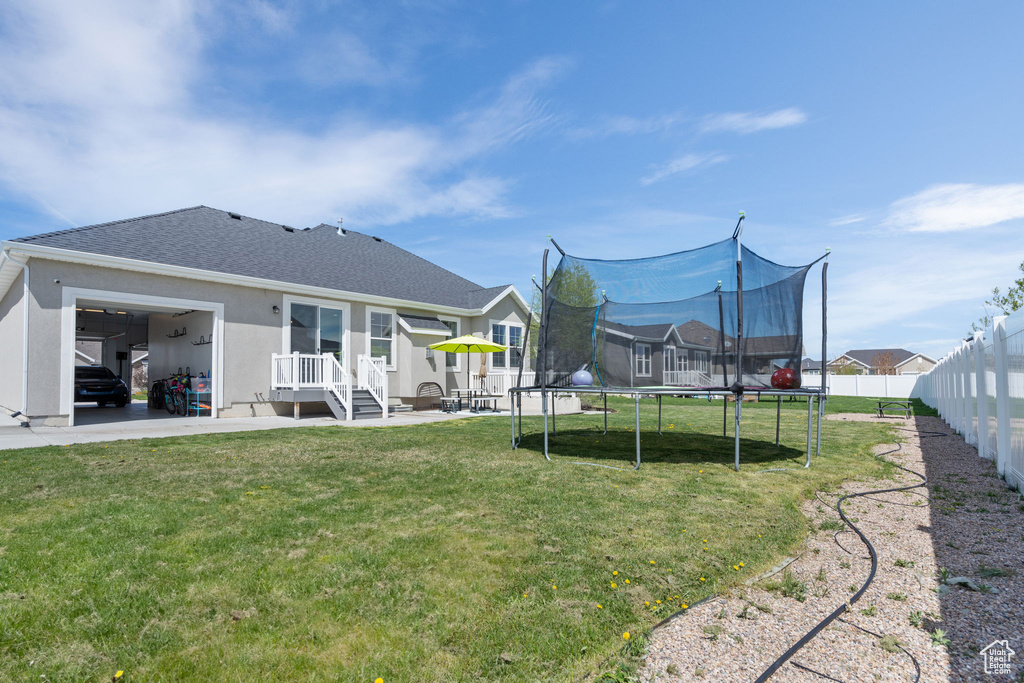Back of property with a trampoline, a lawn, and a patio area