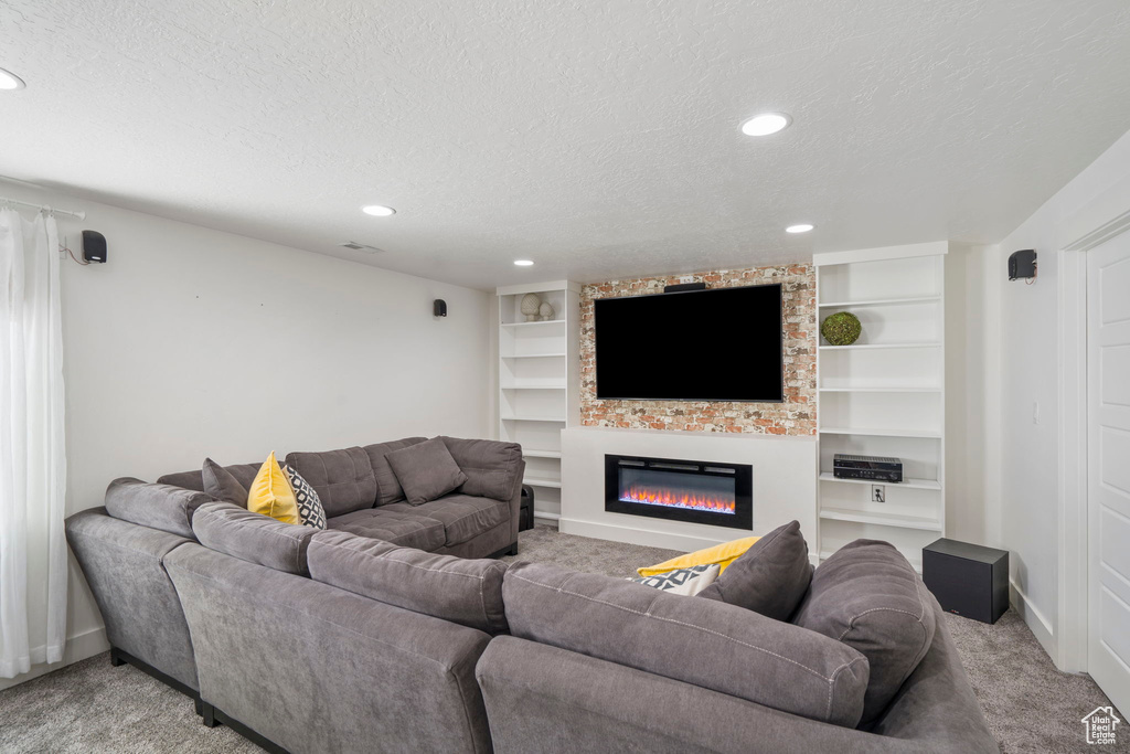 Living room featuring a large fireplace, built in shelves, carpet floors, and a textured ceiling