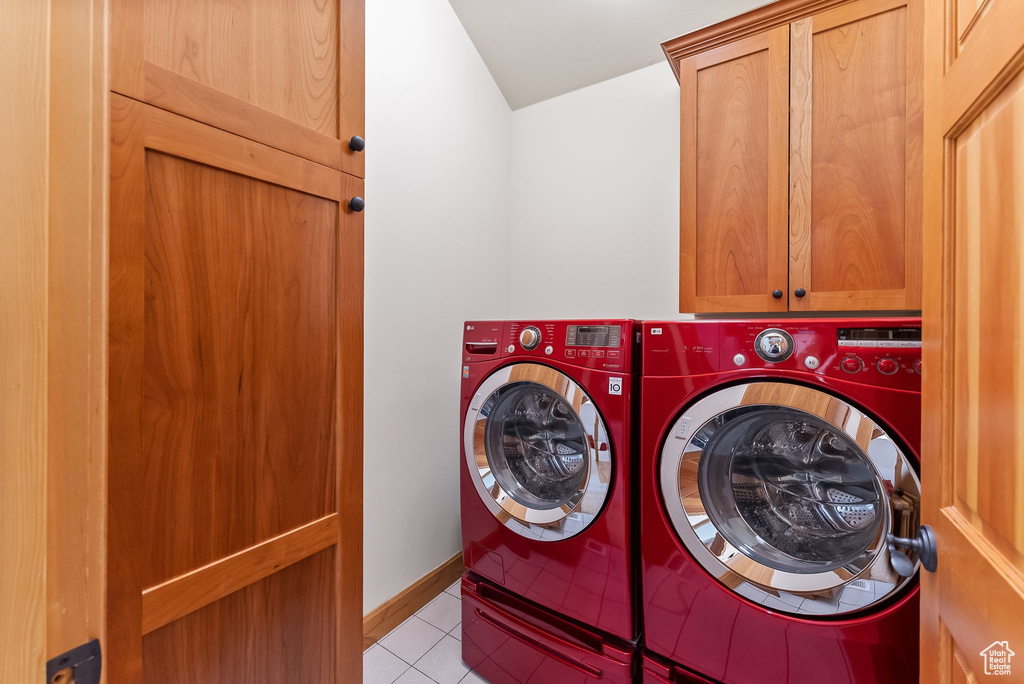 Clothes washing area with cabinets, light tile floors, and washing machine and clothes dryer