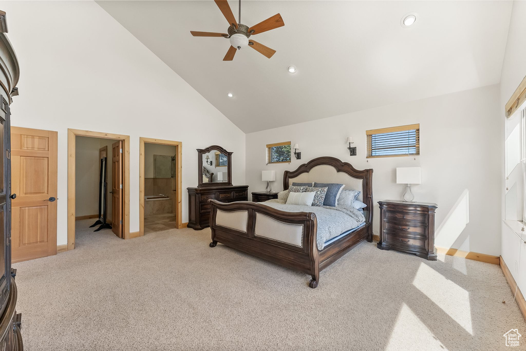 Carpeted bedroom with connected bathroom, ceiling fan, and high vaulted ceiling
