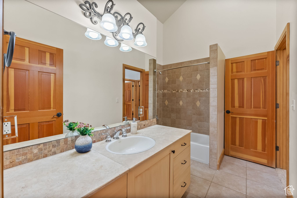 Bathroom featuring tile flooring, tiled shower / bath combo, a notable chandelier, lofted ceiling, and vanity