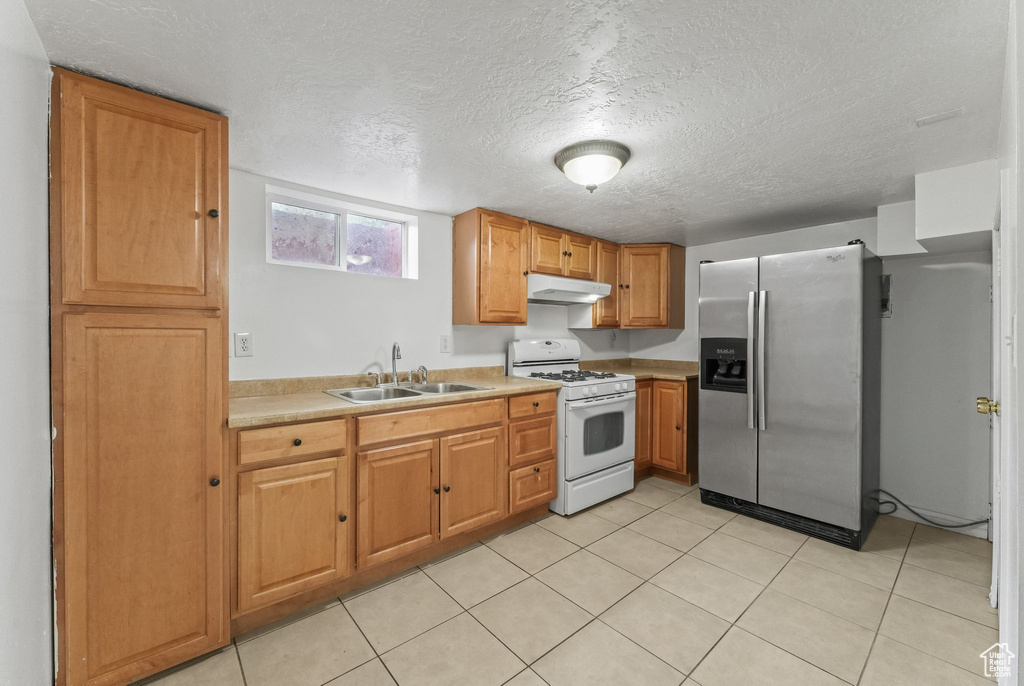 Kitchen with a textured ceiling, stainless steel refrigerator with ice dispenser, white gas stove, sink, and light tile floors