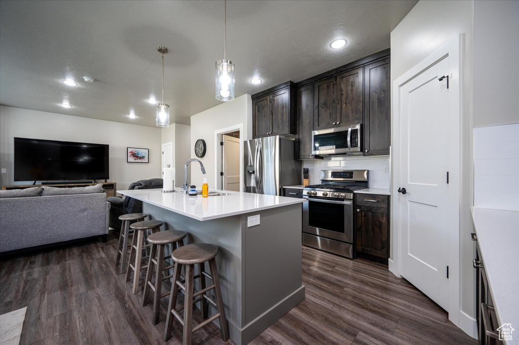 Kitchen featuring appliances with stainless steel finishes, a kitchen bar, sink, dark hardwood / wood-style floors, and a center island with sink