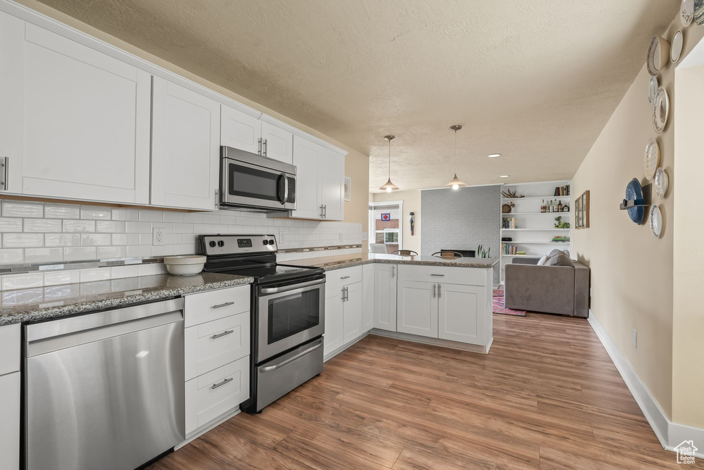 Kitchen featuring white cabinets, kitchen peninsula, light wood-type flooring, and stainless steel appliances