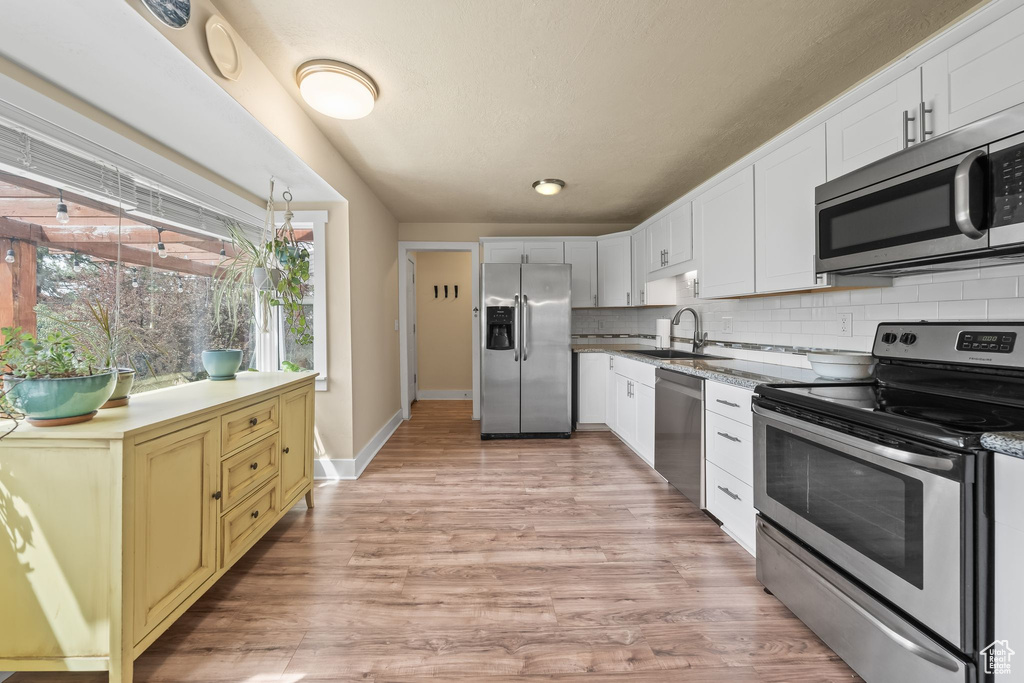Kitchen featuring light hardwood / wood-style floors, appliances with stainless steel finishes, backsplash, and sink