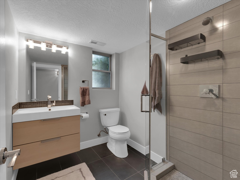 Bathroom with a shower with door, oversized vanity, toilet, a textured ceiling, and tile floors