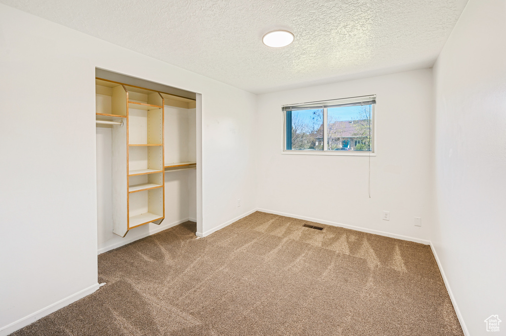 Unfurnished bedroom featuring a textured ceiling, a closet, and carpet floors