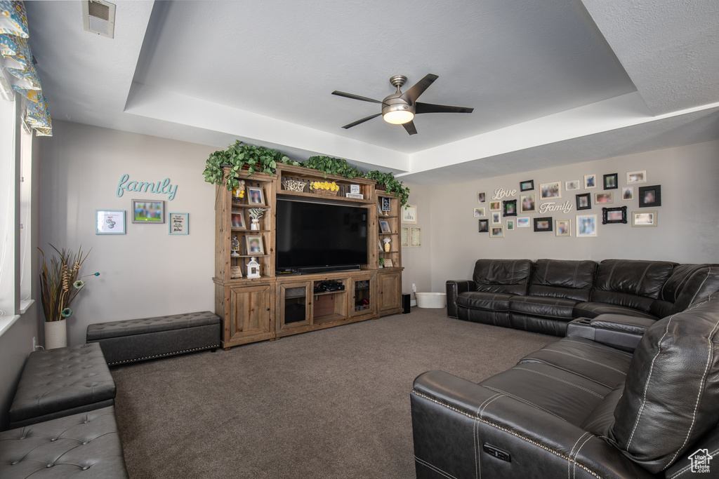 Carpeted living room featuring ceiling fan and a tray ceiling