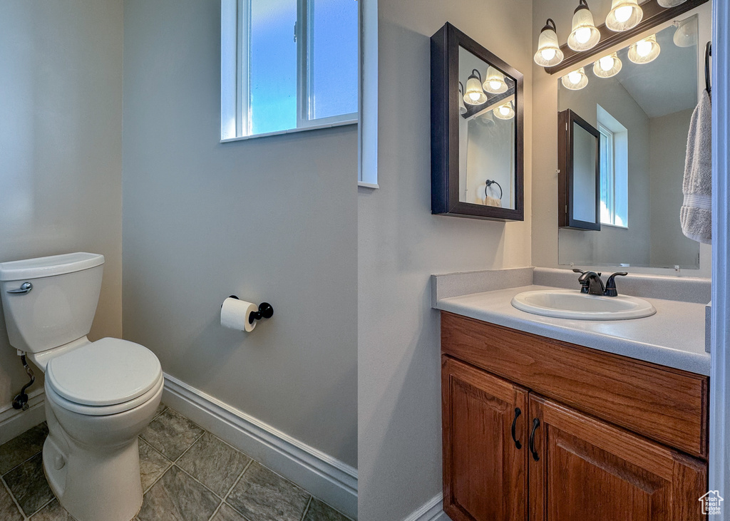 Bathroom featuring vanity with extensive cabinet space, a healthy amount of sunlight, toilet, and tile flooring