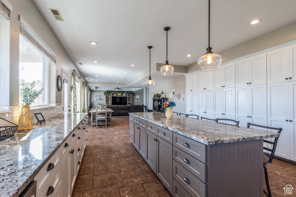 Kitchen featuring dark tile floors, a center island, white cabinetry, a breakfast bar area, and pendant lighting