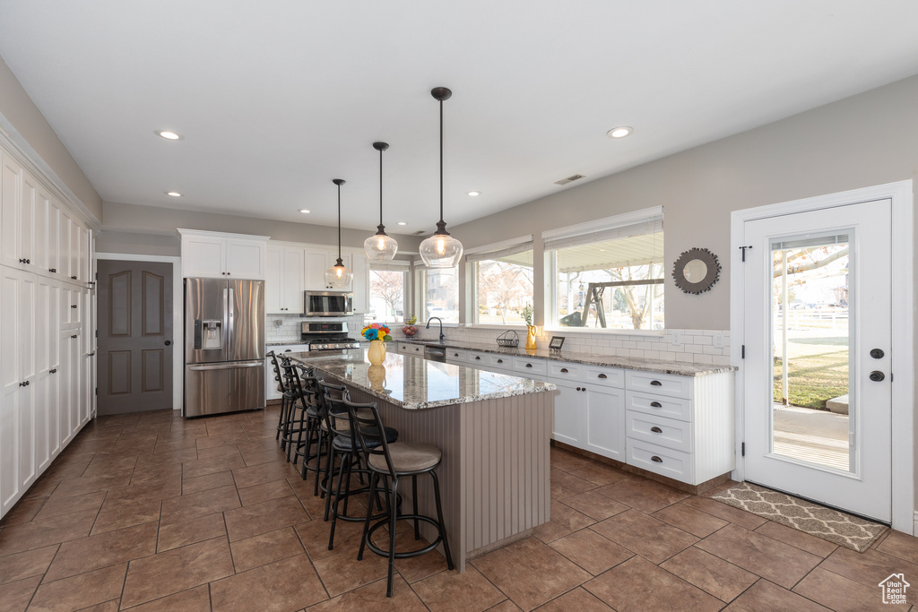 Kitchen featuring backsplash, stainless steel appliances, a center island, and light stone counters
