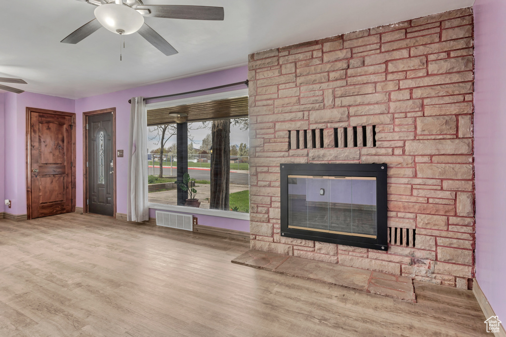 Unfurnished living room featuring a stone fireplace, light hardwood / wood-style flooring, and ceiling fan