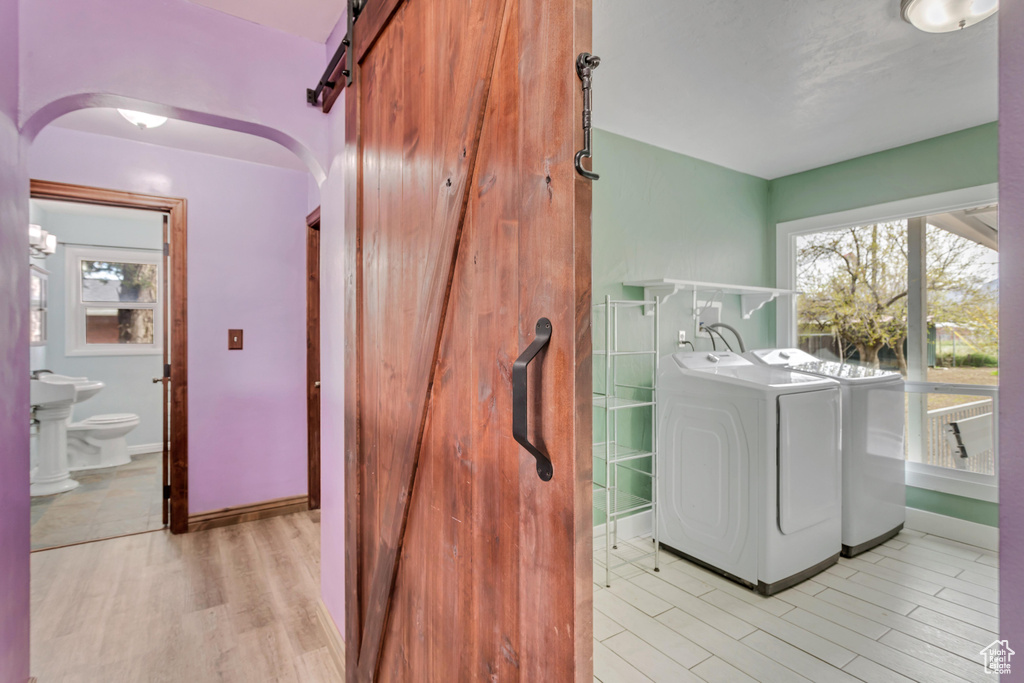 Clothes washing area featuring light hardwood / wood-style flooring, independent washer and dryer, and a barn door