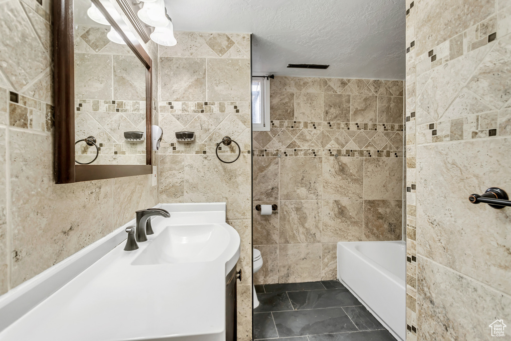Bathroom featuring tile walls, large vanity, toilet, a textured ceiling, and tile floors