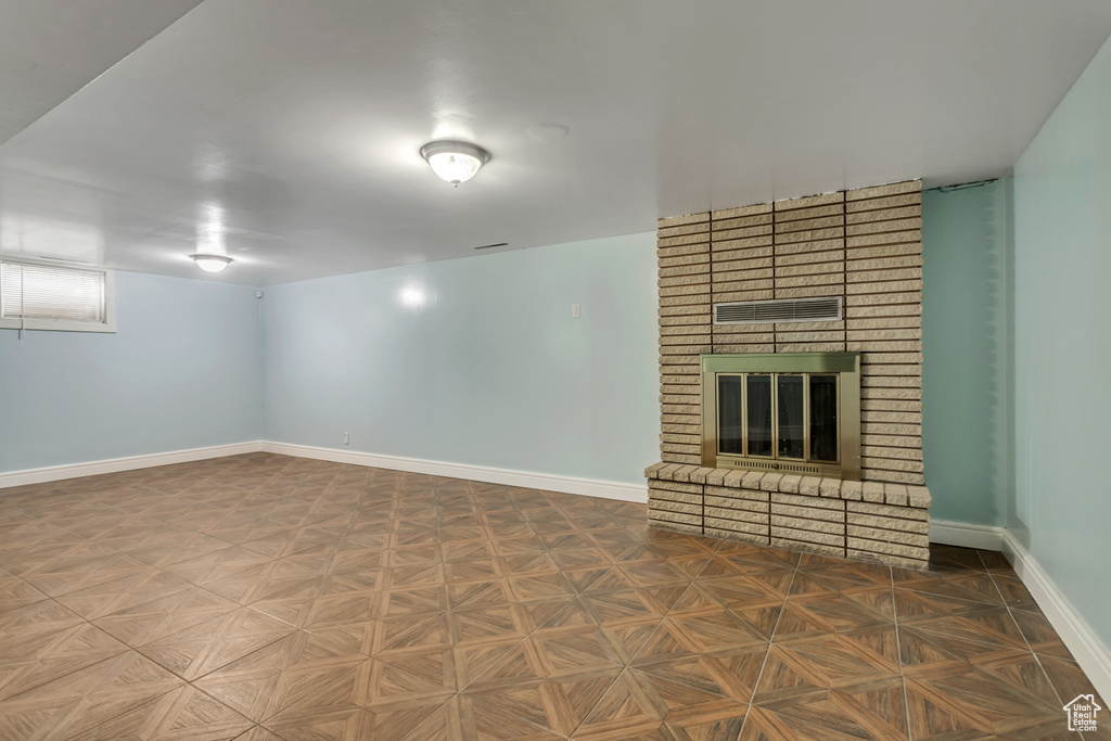 Unfurnished living room featuring brick wall, a brick fireplace, and parquet floors