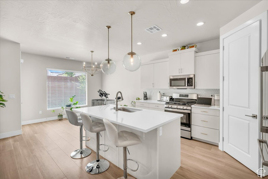 Kitchen featuring hanging light fixtures, stainless steel appliances, tasteful backsplash, white cabinetry, and sink
