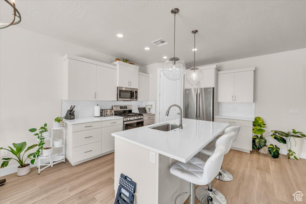 Kitchen featuring tasteful backsplash, light wood-type flooring, stainless steel appliances, and white cabinetry
