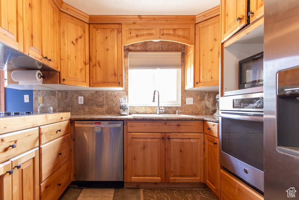 Kitchen with tasteful backsplash, dark tile flooring, stainless steel appliances, and sink